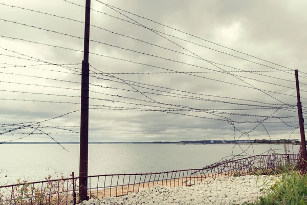 Barb wire omheining over grijze lucht en zee — Stockfoto