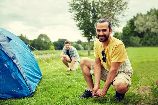 Amigos sorridentes montando tenda ao ar livre — Fotografia de Stock