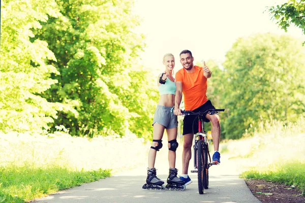 Casal em patins e bicicleta mostrando polegares para cima — Fotografia de Stock