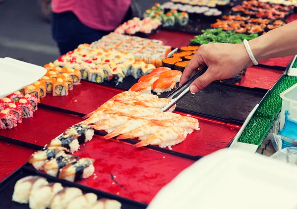 Close up of hand with tongs taking sushi — Stock Photo, Image