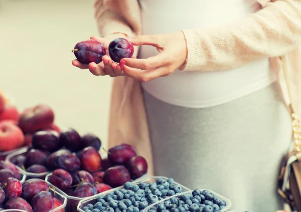 pregnant woman choosing plums at street market