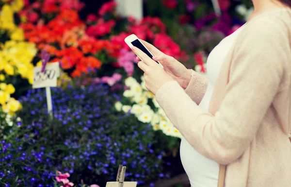 Беременная женщина со смартфоном на цветочном рынке — стоковое фото
