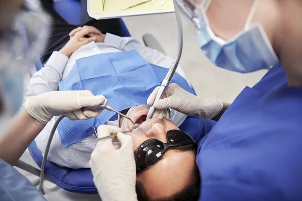 Dentista feminino tratando os dentes dos pacientes do sexo masculino — Fotografia de Stock
