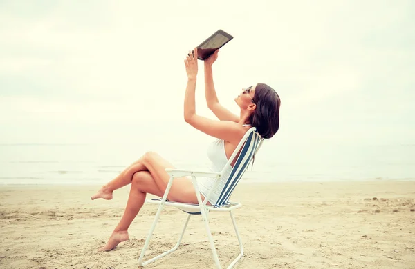 Счастливая женщина с планшетным компьютером, делающая селфи на пляже — стоковое фото