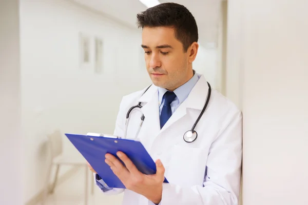 Doctor writing to clipboard at hospital — Stock Photo, Image