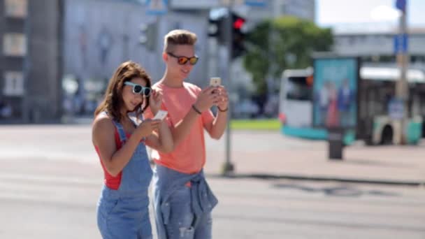 Feliz pareja adolescente con teléfonos inteligentes en la ciudad — Vídeos de Stock