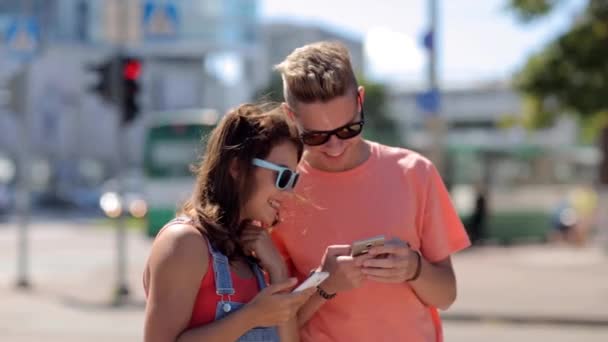 Feliz pareja adolescente con teléfonos inteligentes en la ciudad — Vídeos de Stock