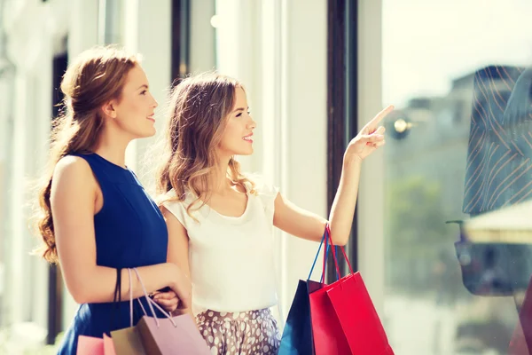 Happy women with shopping bags at shop window — Stock Photo, Image