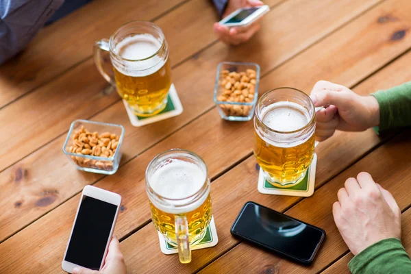 Close up de mãos com smartphones e cerveja no bar — Fotografia de Stock