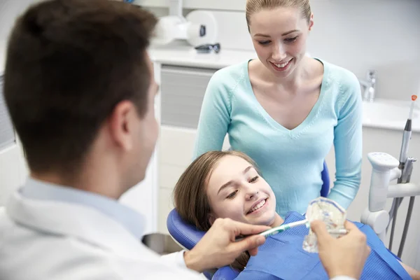Dentista feliz mostrando cepillo de dientes a chica paciente —  Fotos de Stock