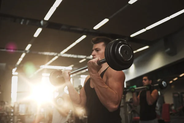 Hombres jóvenes flexionando los músculos con las barras en el gimnasio — Foto de Stock