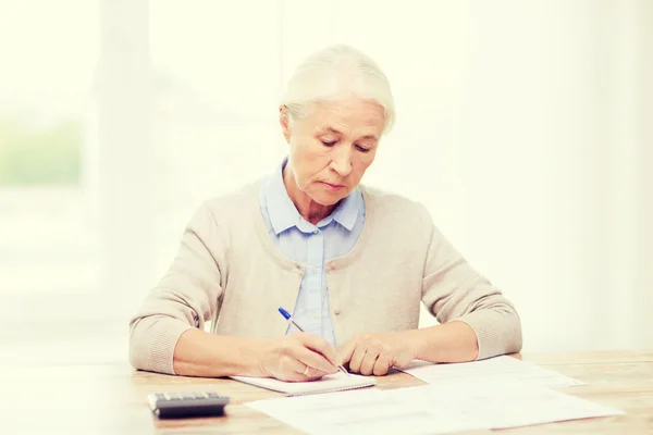 Mulher idosa com papéis e calculadora em casa — Fotografia de Stock