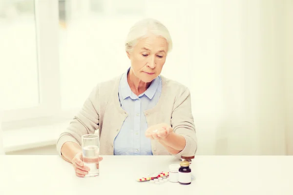 Senior woman with water and medicine at home — Stock Photo, Image