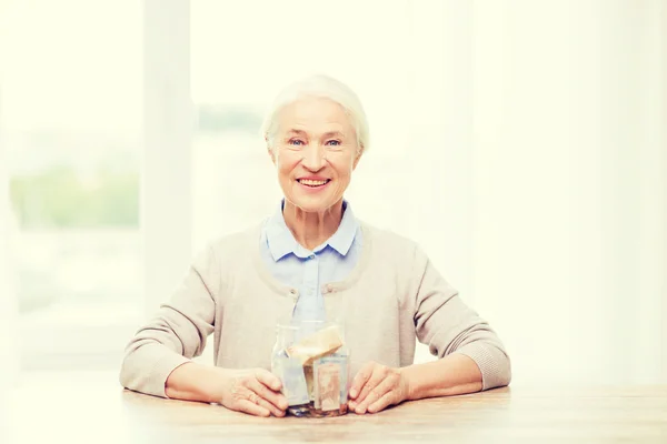 Seniorin mit Geld im Glas zu Hause — Stockfoto