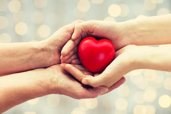 Seniores e jovens mãos de mulher segurando coração vermelho — Fotografia de Stock