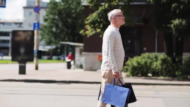 Äldre man med påsar promenader i city — Stockvideo