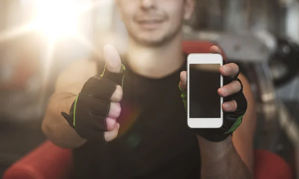 Junger Mann mit Smartphone zeigt im Fitnessstudio Daumen hoch — Stockfoto