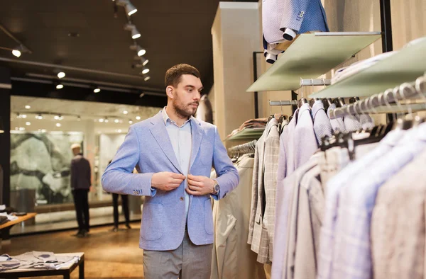 Happy young man trying jacket on in clothing store — Stock Photo, Image