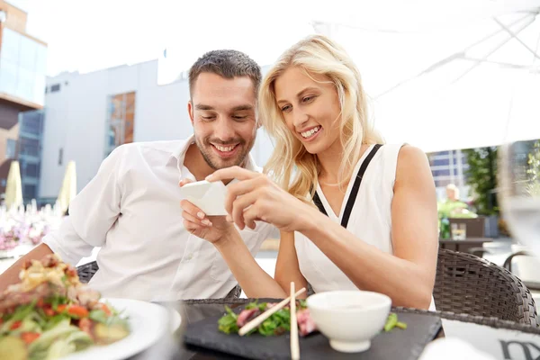 Счастливая пара со смартфоном на террасе ресторана — стоковое фото
