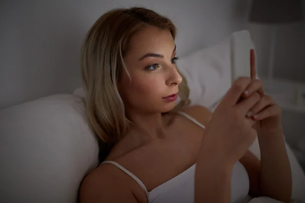 Jeune femme avec smartphone dans le lit à la maison chambre — Photo