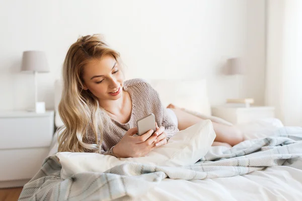 Heureuse jeune femme avec smartphone au lit à la maison — Photo