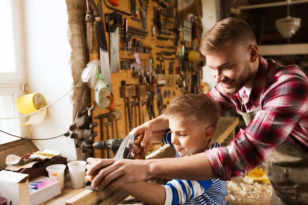 Father and son with plane shaving wood at workshop — Stock Photo, Image