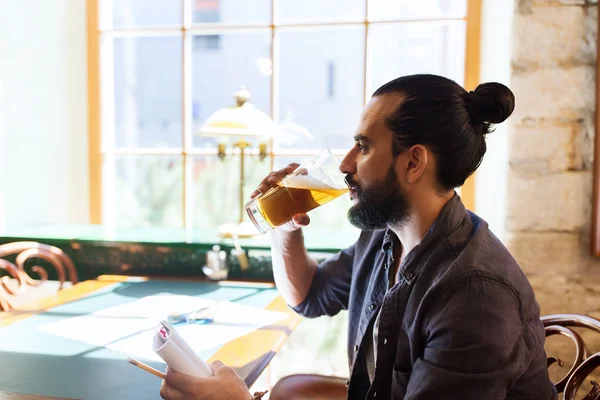 Человек с блокнотом пьет пиво в баре или пабе — стоковое фото