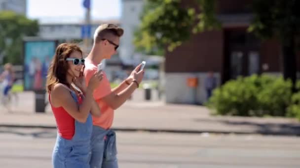 Feliz pareja adolescente con teléfonos inteligentes en la ciudad — Vídeos de Stock