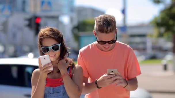 Feliz pareja adolescente con teléfonos inteligentes en la ciudad — Vídeos de Stock