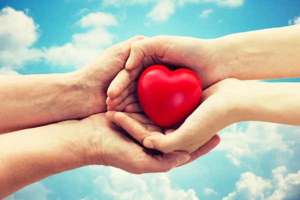 Anziani e giovani mani donna tenendo il cuore rosso — Foto Stock