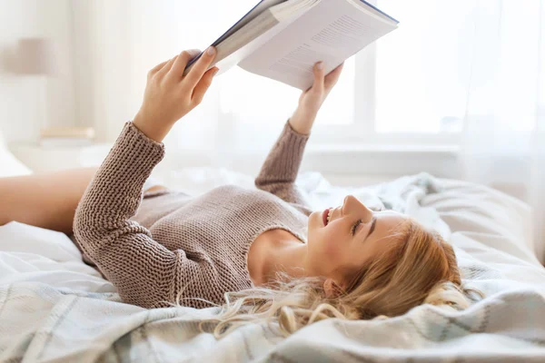 Evde yatakta kitap okuyan genç bir kadın. — Stok fotoğraf