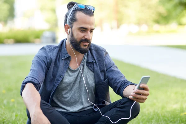 Hombre con auriculares y teléfono inteligente sentado en la hierba — Foto de Stock