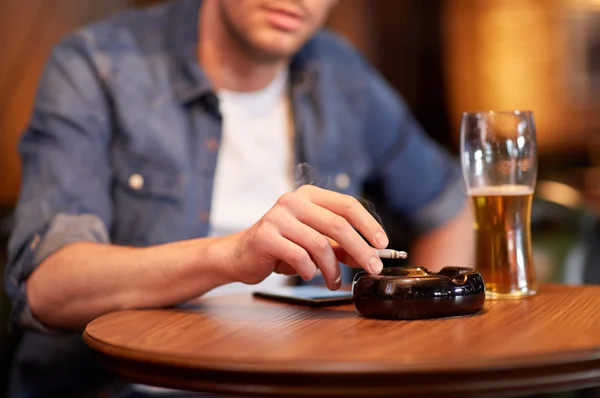 Чоловік п'є пиво і курить сигарету в барі — стокове фото