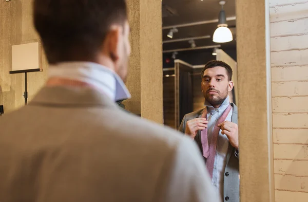 Muž vázání kravaty na na zrcadlo v obchod s oblečením — Stock fotografie