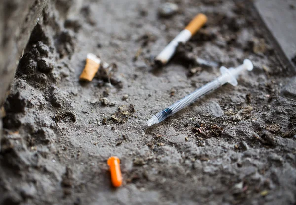 Detailní záběr z injekční stříkačky a uzené cigaret na zemi — Stock fotografie