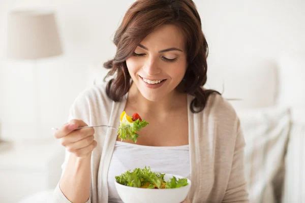 Sonriente joven mujer comiendo ensalada en casa —  Fotos de Stock