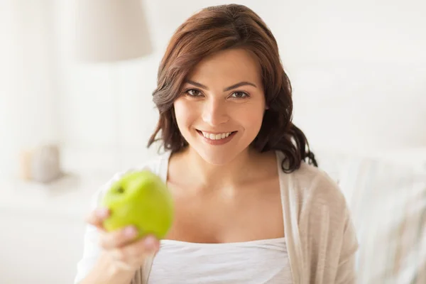Sorridente giovane donna mangiare mela verde a casa — Foto Stock