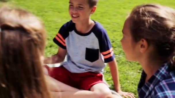 Группа счастливых детей, сидящих на траве и разговаривающих — стоковое видео