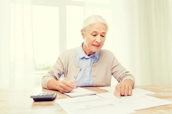 Старша жінка з паперами і калькулятором вдома — стокове фото
