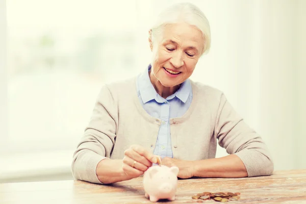 Senior woman putting money to piggy bank at home — Stock Photo, Image