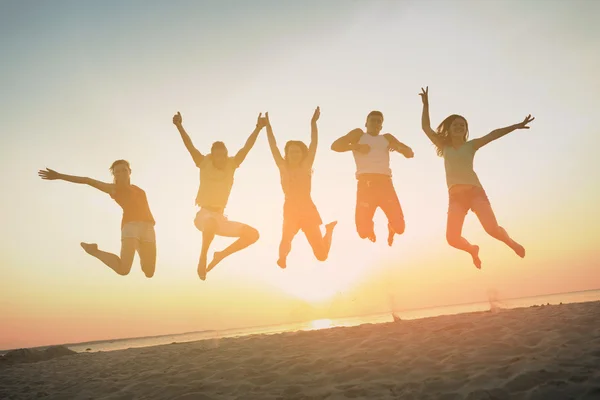 Lachende vrienden dansen en springen op strand — Stockfoto