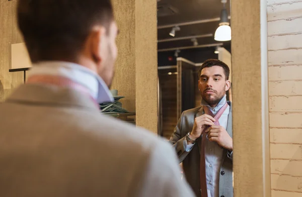 Hombre atando corbata en el espejo en tienda de ropa — Foto de Stock