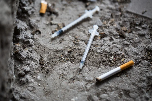 Zbliżenie na strzykawkę i wędzone papierosa na ziemi — Zdjęcie stockowe