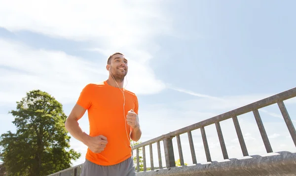 Happy man with earphones running outdoors — Stock Photo, Image