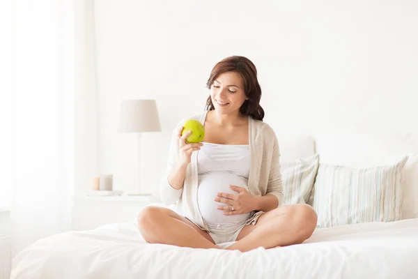 Happy pregnant woman eating green apple at home — Stock Photo, Image