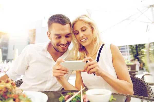 Happy couple with smatphone at restaurant terrace — Stock Photo, Image