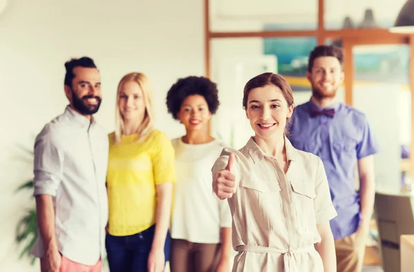 Mujer mostrando pulgares hacia arriba sobre el equipo de oficina creativa — Foto de Stock