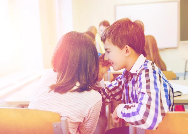 Glimlachend schoolmeisje aan klasgenoot oor fluisteren — Stockfoto