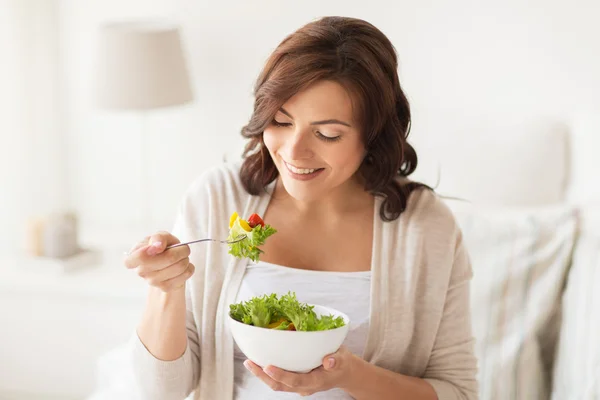 Lachende jonge vrouw salade eten thuis — Stockfoto