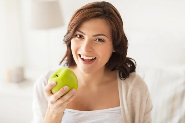 Sorrindo jovem mulher comendo maçã verde em casa — Fotografia de Stock